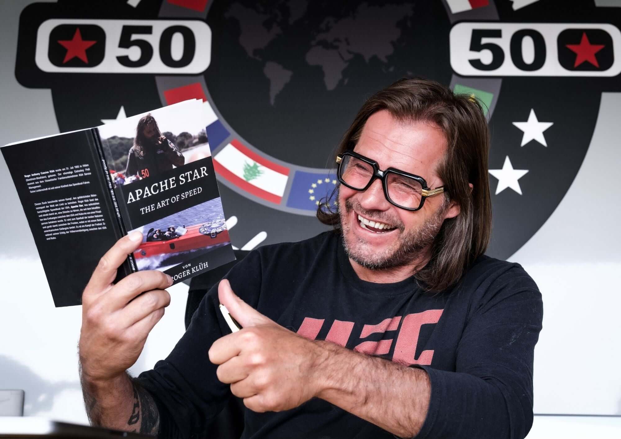 Roger Klüh proudly holding his book Apache Star: "The Art of Speed" with a thumbs-up.
