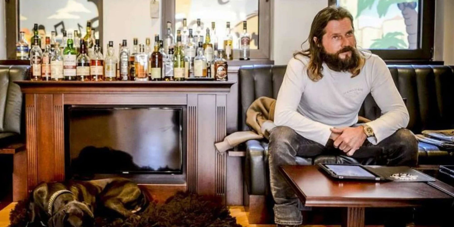 Roger Anthony Cassius Klüh from Düsseldorf sits in cigar lounge with liquor bottles and dog.