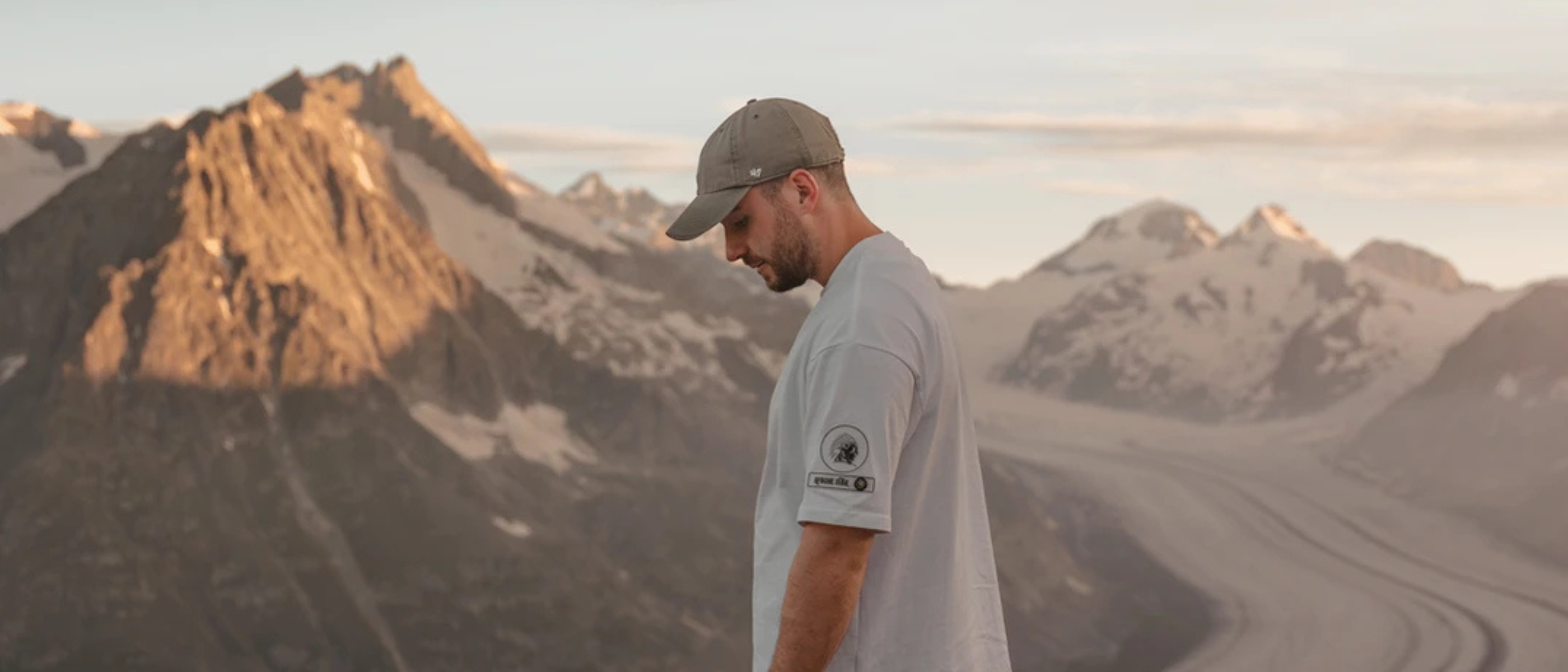 Man wearing a casual T-shirt and cap in scenic mountain landscape by iconic APACHE STAR Designer Luxury T-Shirts from PFW.