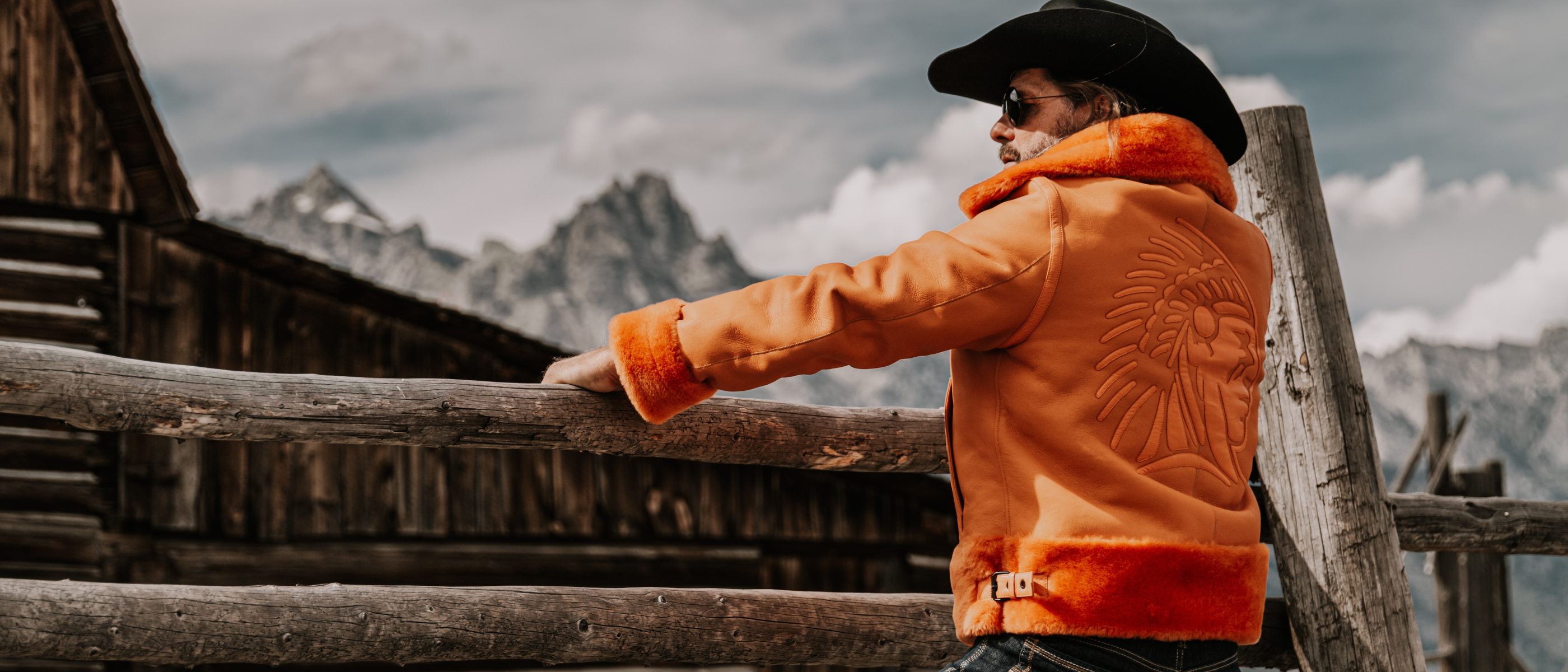 Brand owner Roger Klüh in APACHE orange Toskana lamb aviator jacket by APACHE STAR and cowboy hat gazes at mountain horizon in Wyoming.