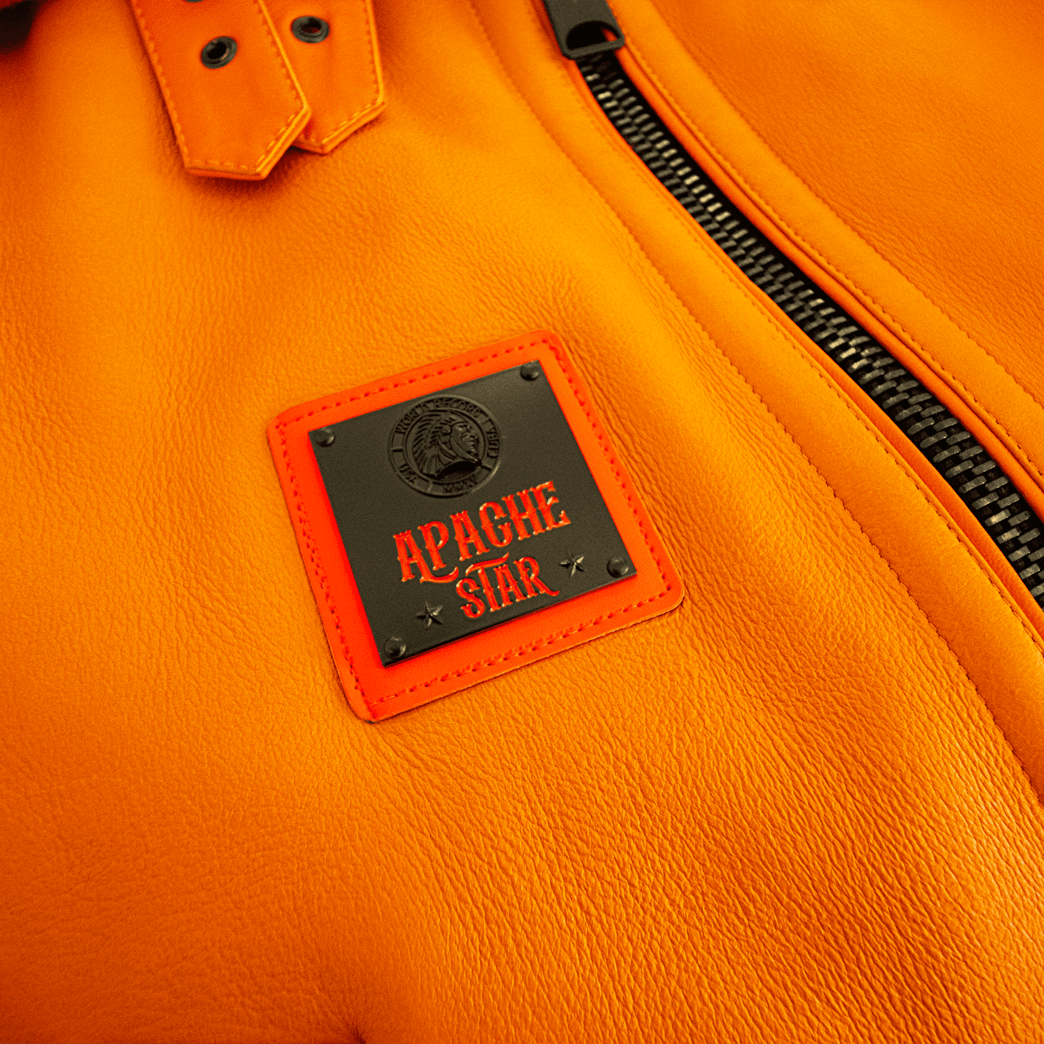 Close-up of FLAMING AVIATOR by APACHE STAR leather patch on Toscana Nappa Lamb Pilot Jacket. Premium branding detail on vibrant orange outerwear.