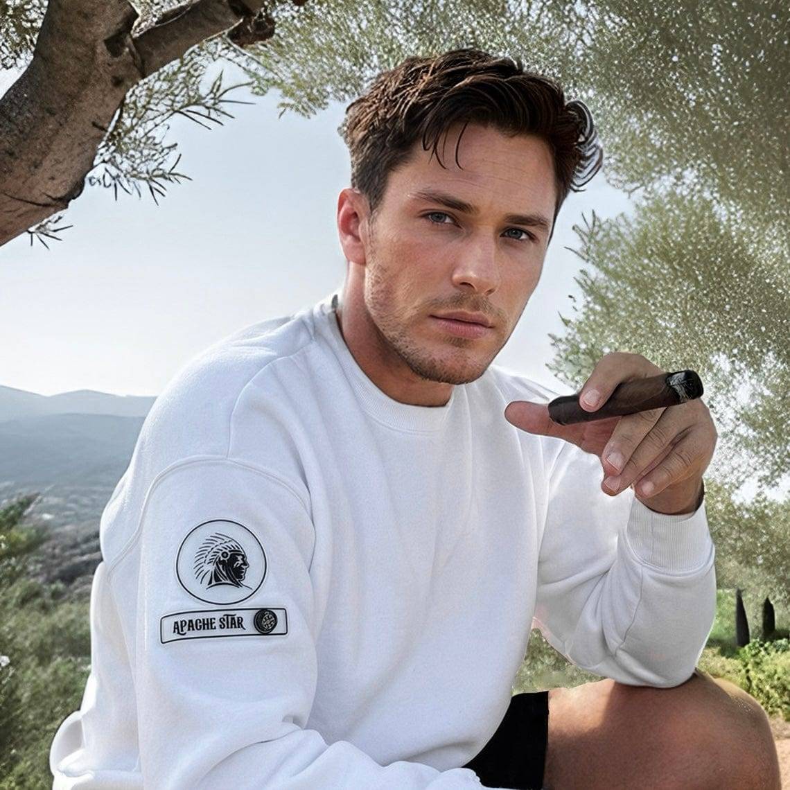 Monaco Sweatshirt in white by APACHE STAR, worn by man outdoors with cigar. Features fleece lining and compass patch on sleeve.