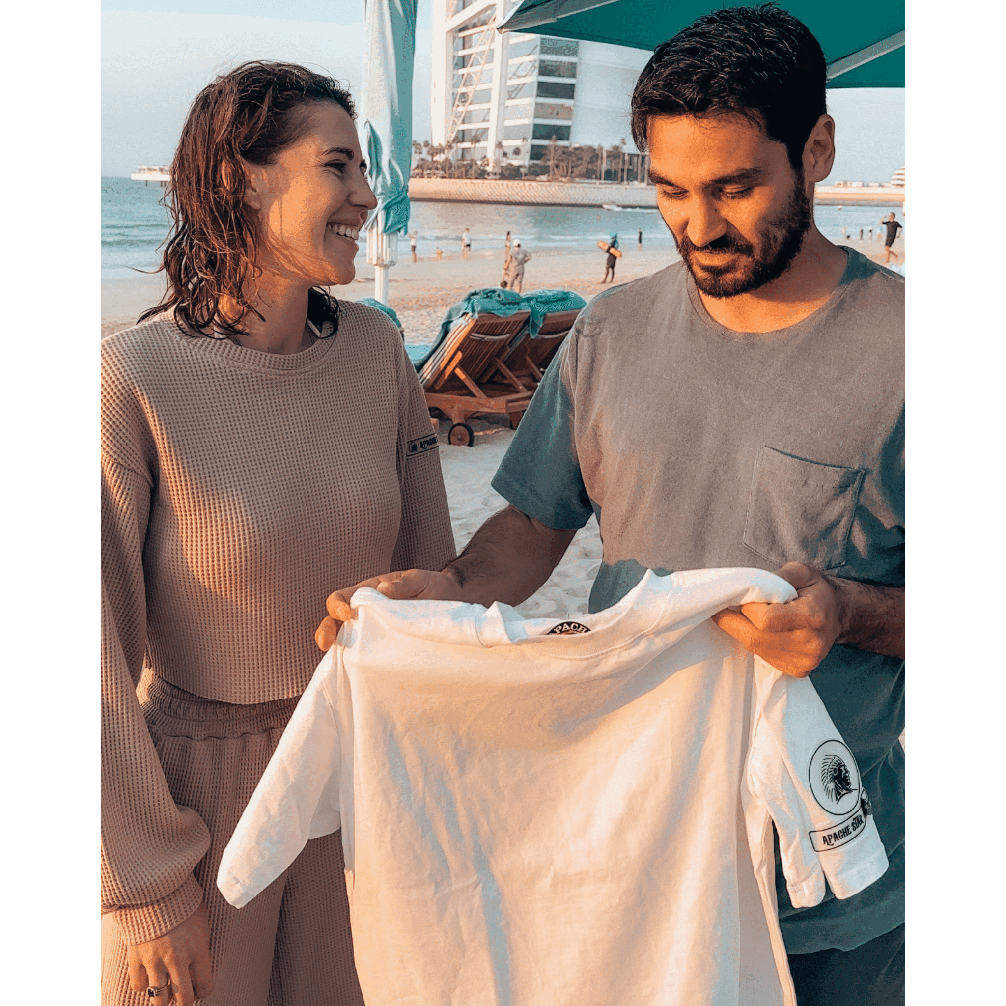Ilkay Gündogan & Jessica Frühbrodt admiring white Iconic APACHE STAR Miami Tee, emphasizing sustainable design and versatile unisex appeal.