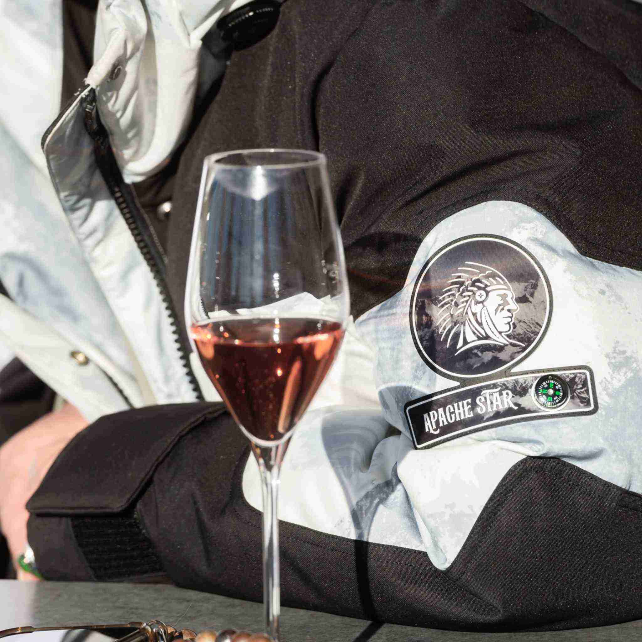Lifestyle shot of Submerged Sentry white down coat sleeve with APACHE STAR logo beside a glass of rosé, blending luxury and function.