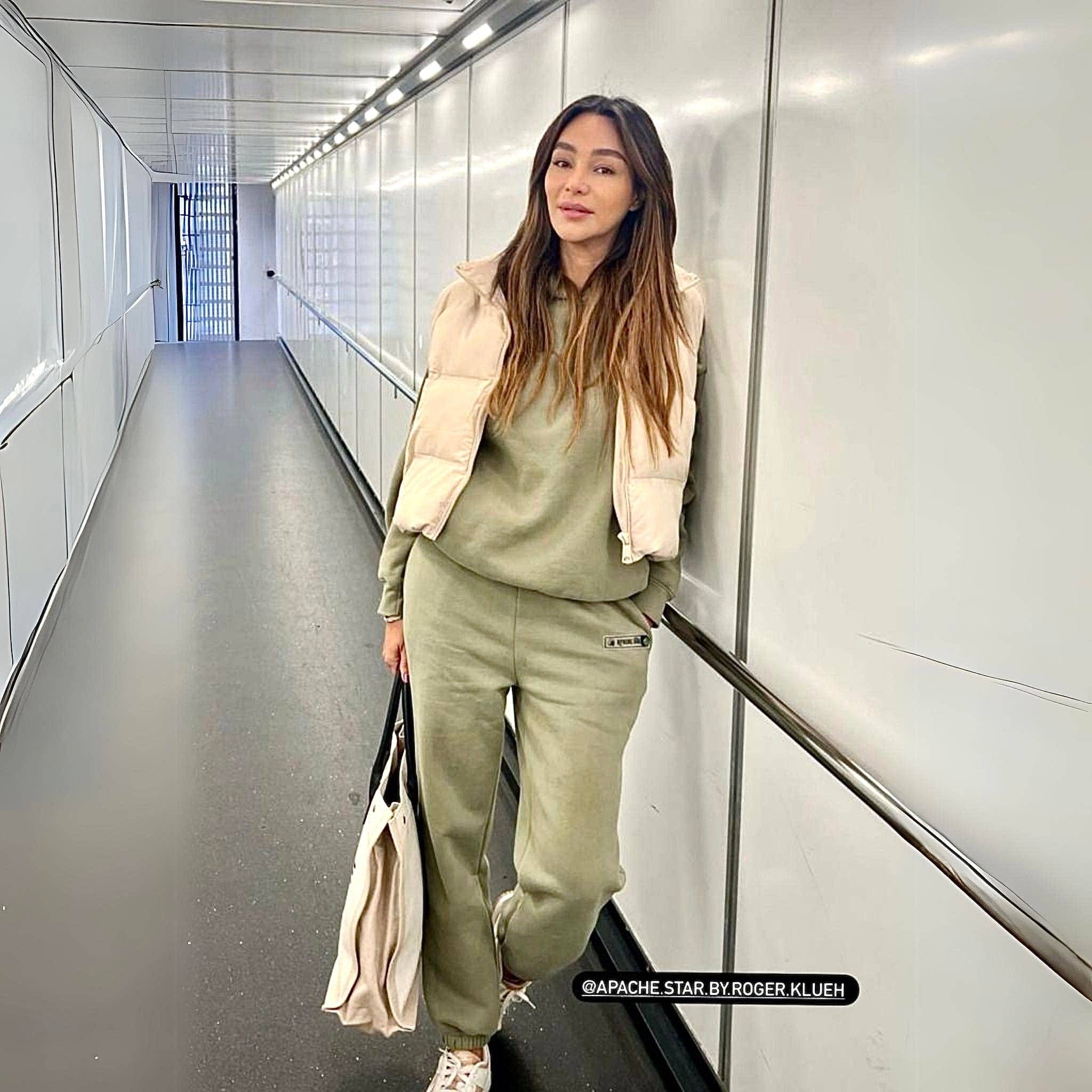 Monaco Sweatshirt in military green by APACHE STAR, styled with matching joggers. Worn by Verona Pooth in airport corridor, showcasing travel-ready comfort.