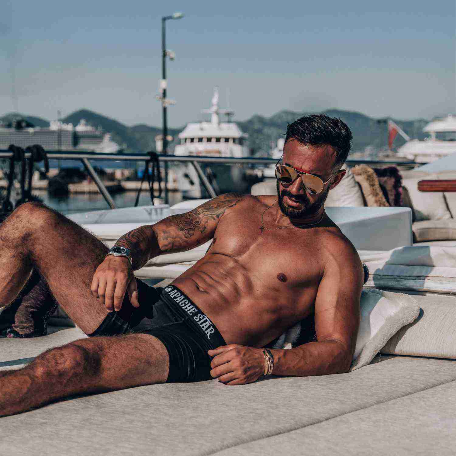 Man lounging on boat in black boxer briefs at marina