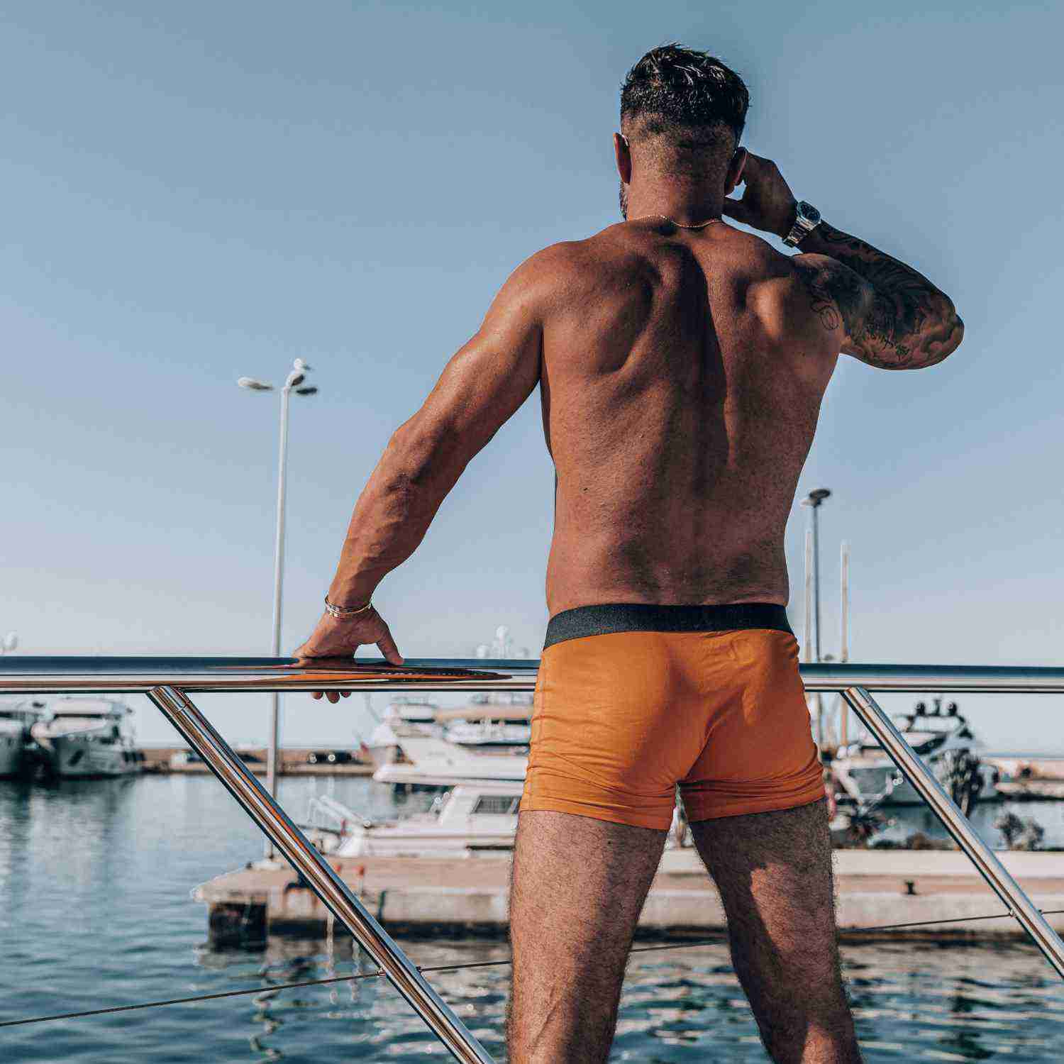 COMMANDER'S COMFORT orange boxer briefs from 3 or 5 pack men's set by APACHE STAR, shown from the back on a yacht, highlighting bold orange color and fit.