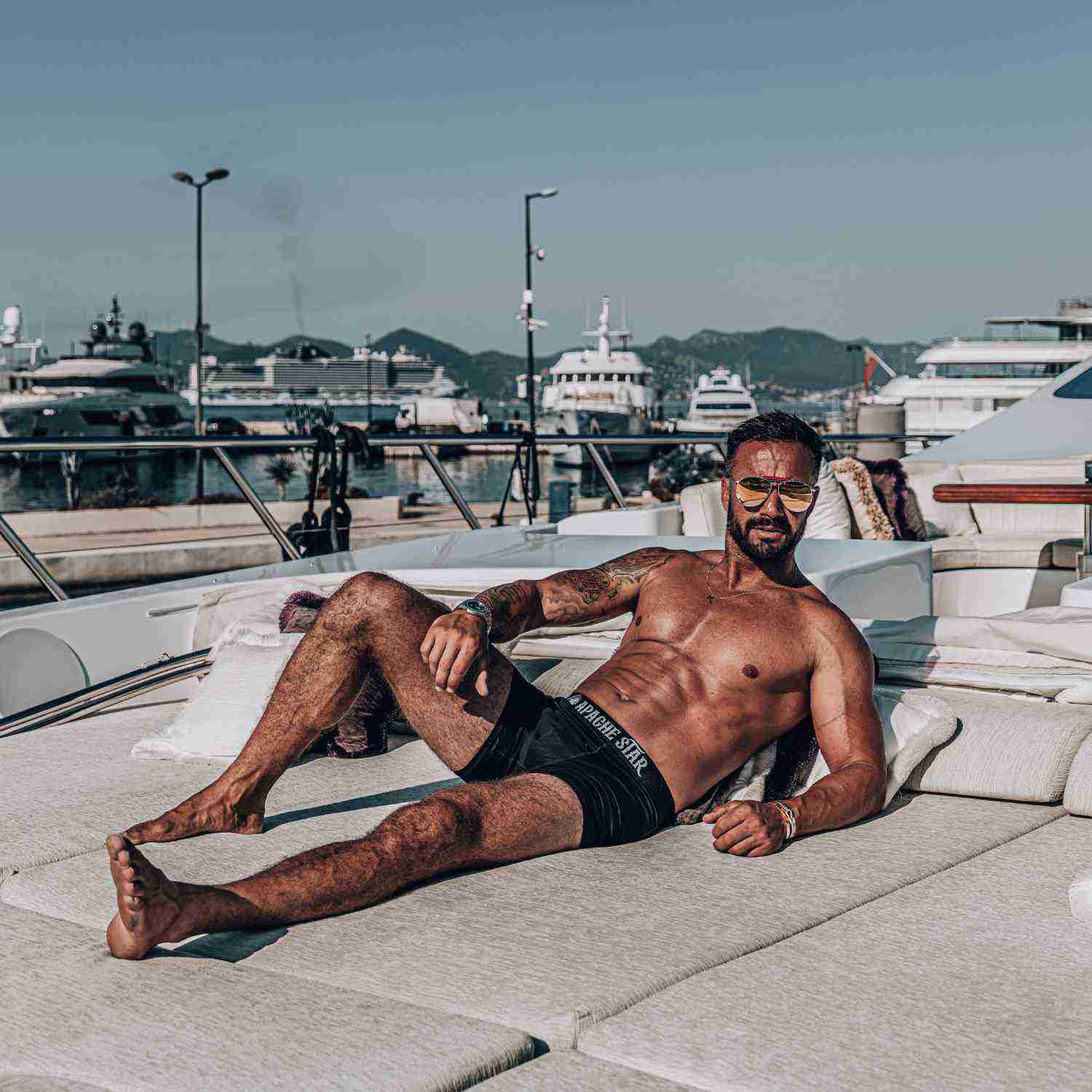 Man with tattoos in orange boxer briefs on boat deck