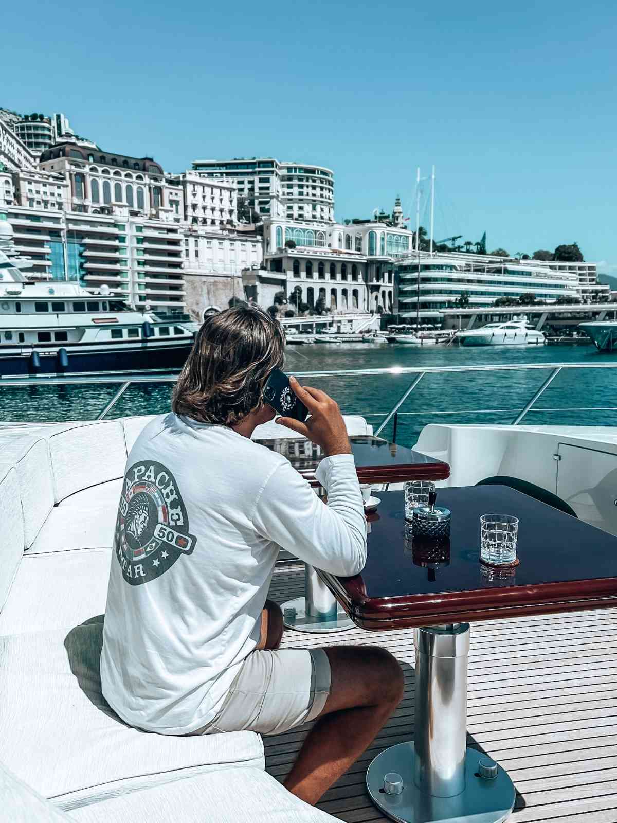 APACHE STAR Clifftop Captain Longsleeve Shirt worn by Roger Klüh on Mangusta yacht on the Côte d´Ázur in South of France, showcasing back logo design by APACHE STAR® in a luxury marina. Ideal for summer activewear.