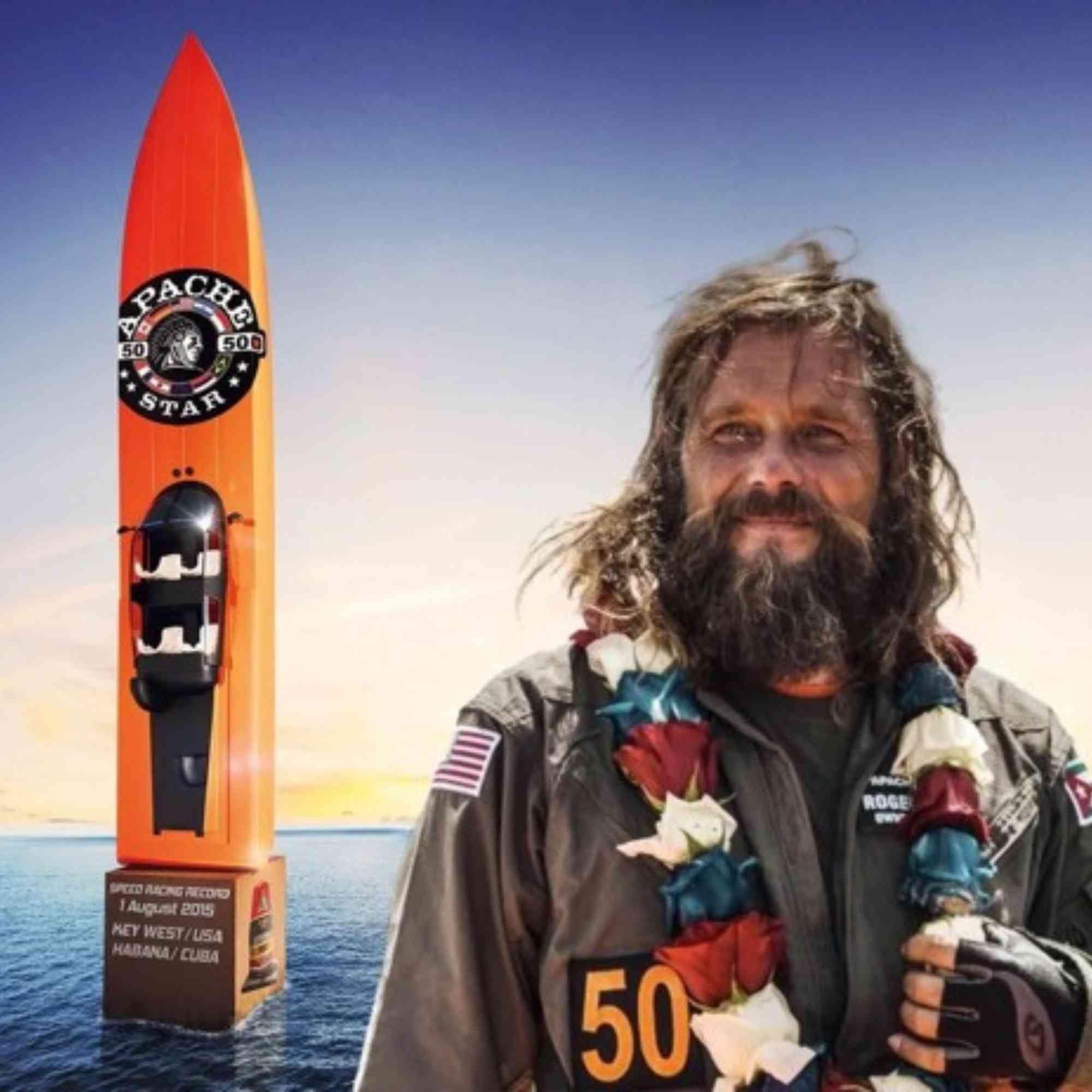 World Record setter Roger Anthony Cassius Klüh wearing a flight suit with the racing number 50 and US American flag patches stands proudly smiling with a flower lei around his neck. Behind him is a large orange rocket-shaped watercraft labeled APACHE STAR®  floating on the ocean. The base of the watercraft displays text indicating a speed world record from Key West, USA to Havana, Cuba on August 1, 2015.
