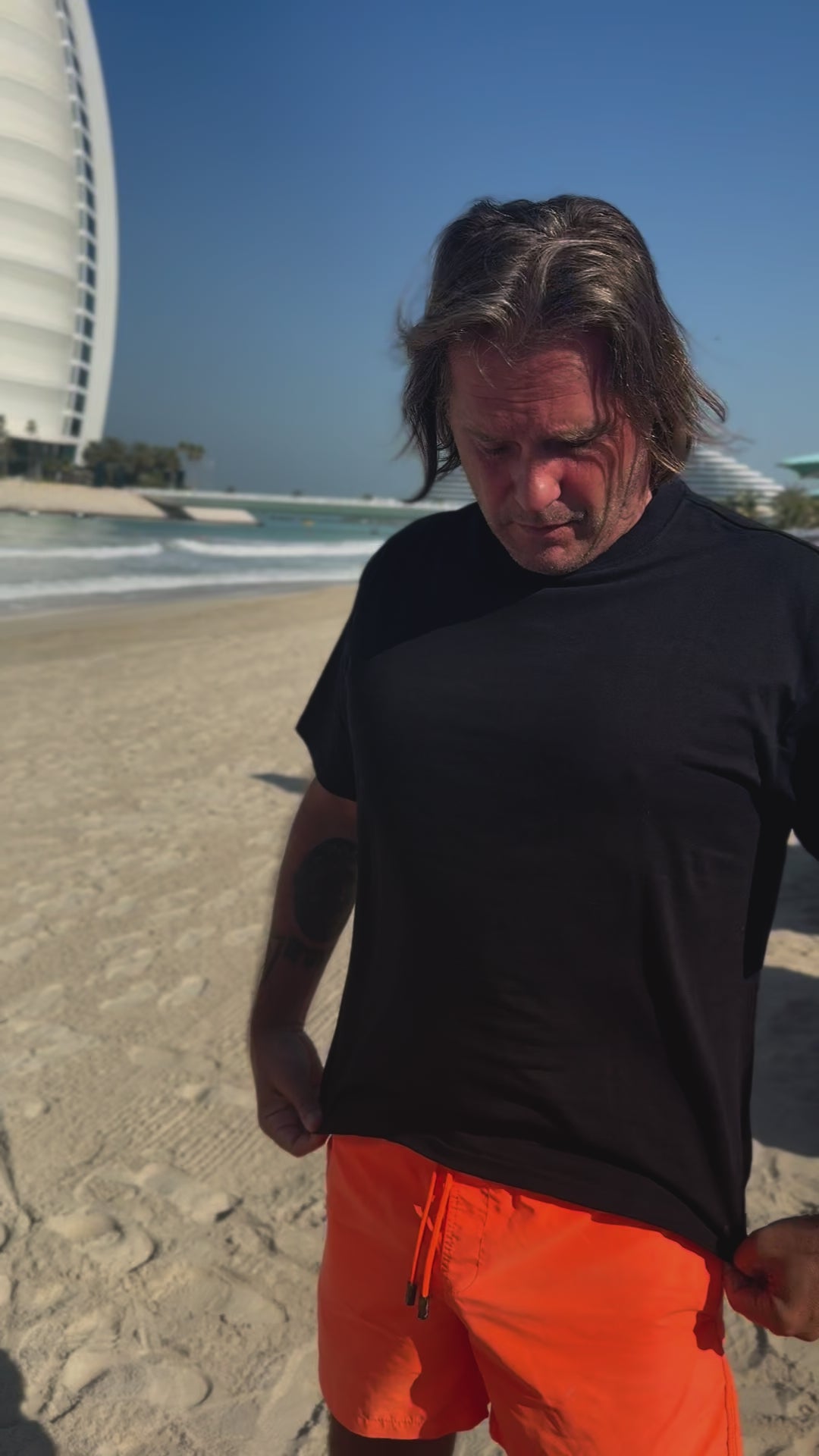 Roger Klüh on the beach wearing black Iconic APACHE STAR Miami Tee, ideal for summer with breathable and anti-wrinkle fabric.