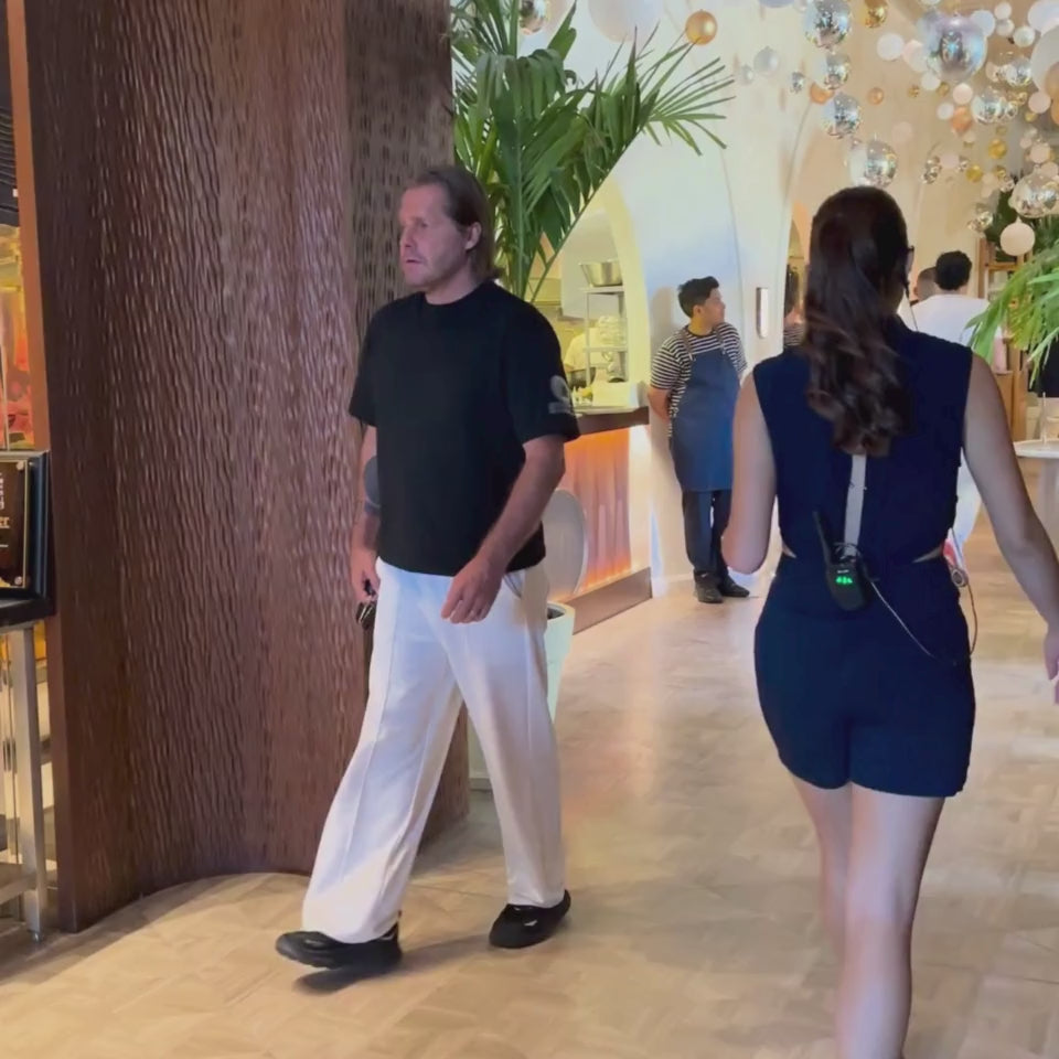 Roger Klüh walking indoors at Nammos Beach Club Dubai in black Iconic APACHE STAR Miami Tee, combining casual elegance with sustainable cotton comfort.