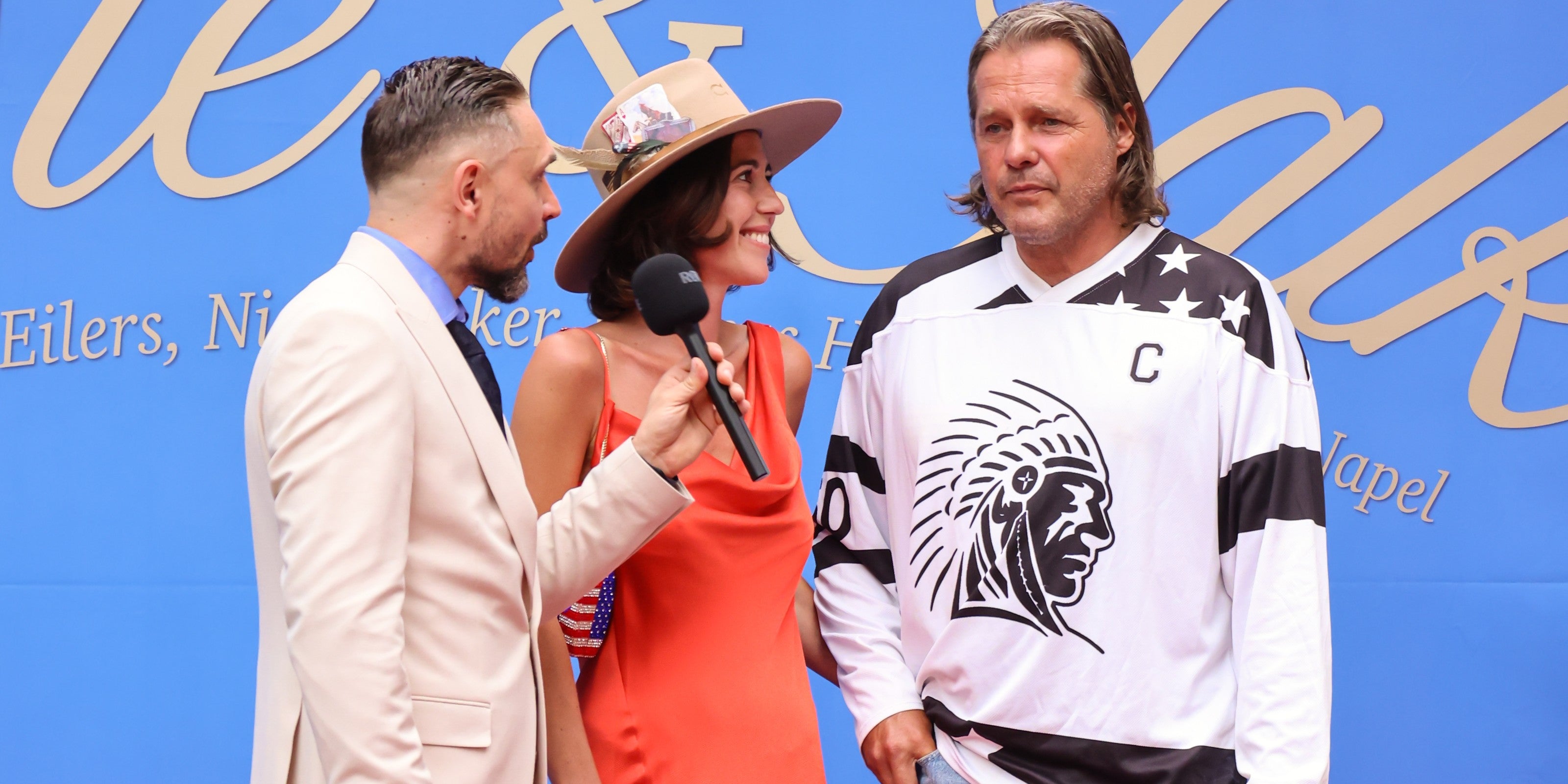 Jessica Frühbrodt, CEO of APACHE STAR®, being interviewed on the red carpet of the Taste & Talk Nightwalk at Schloss Reichenow near Berlin, 21 August 2026, next to a guest in the APACHE STAR® hockey jersey
