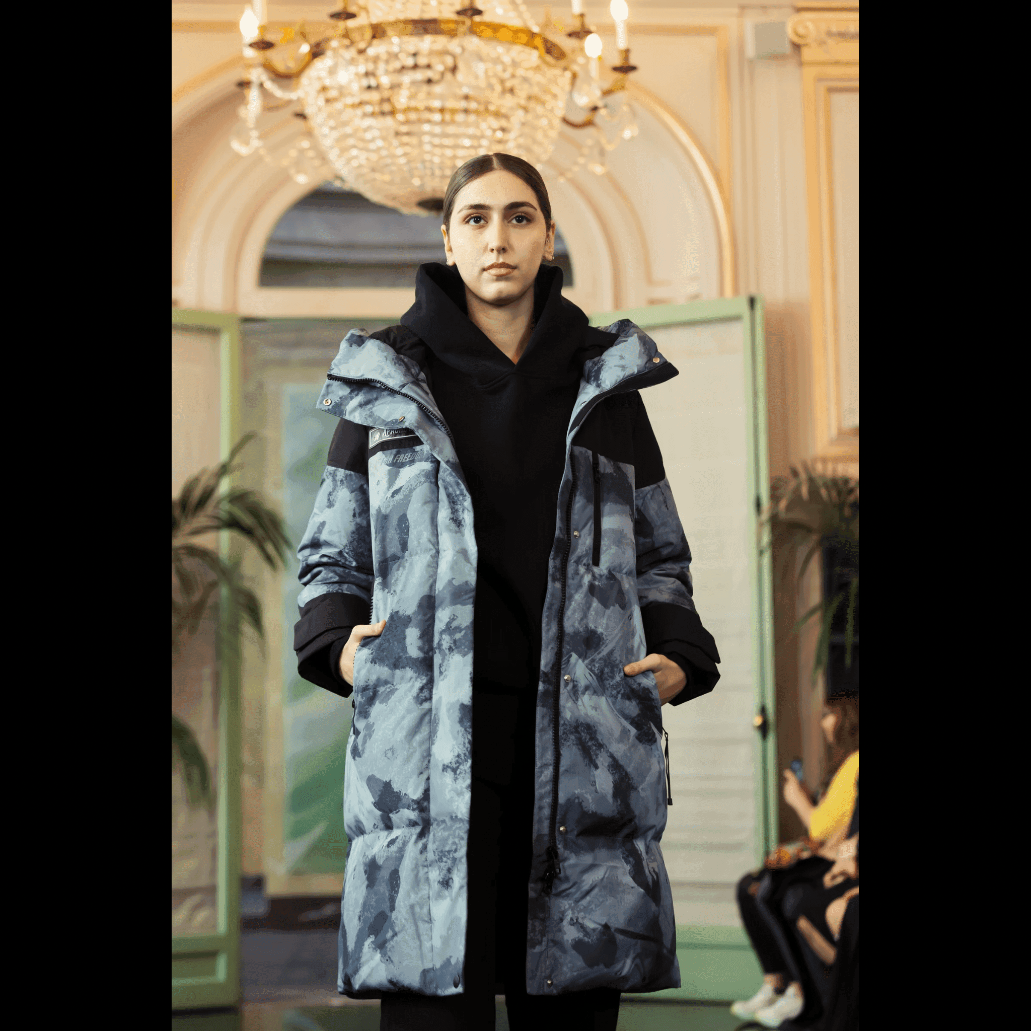 Vintage Down Coat - Blue Camouflage by APACHE STAR | Function, Style, Tech. Close-up of model wearing blue camouflage down coat under chandelier lighting at Paris Fashion Week featured in print magazine Elle.
