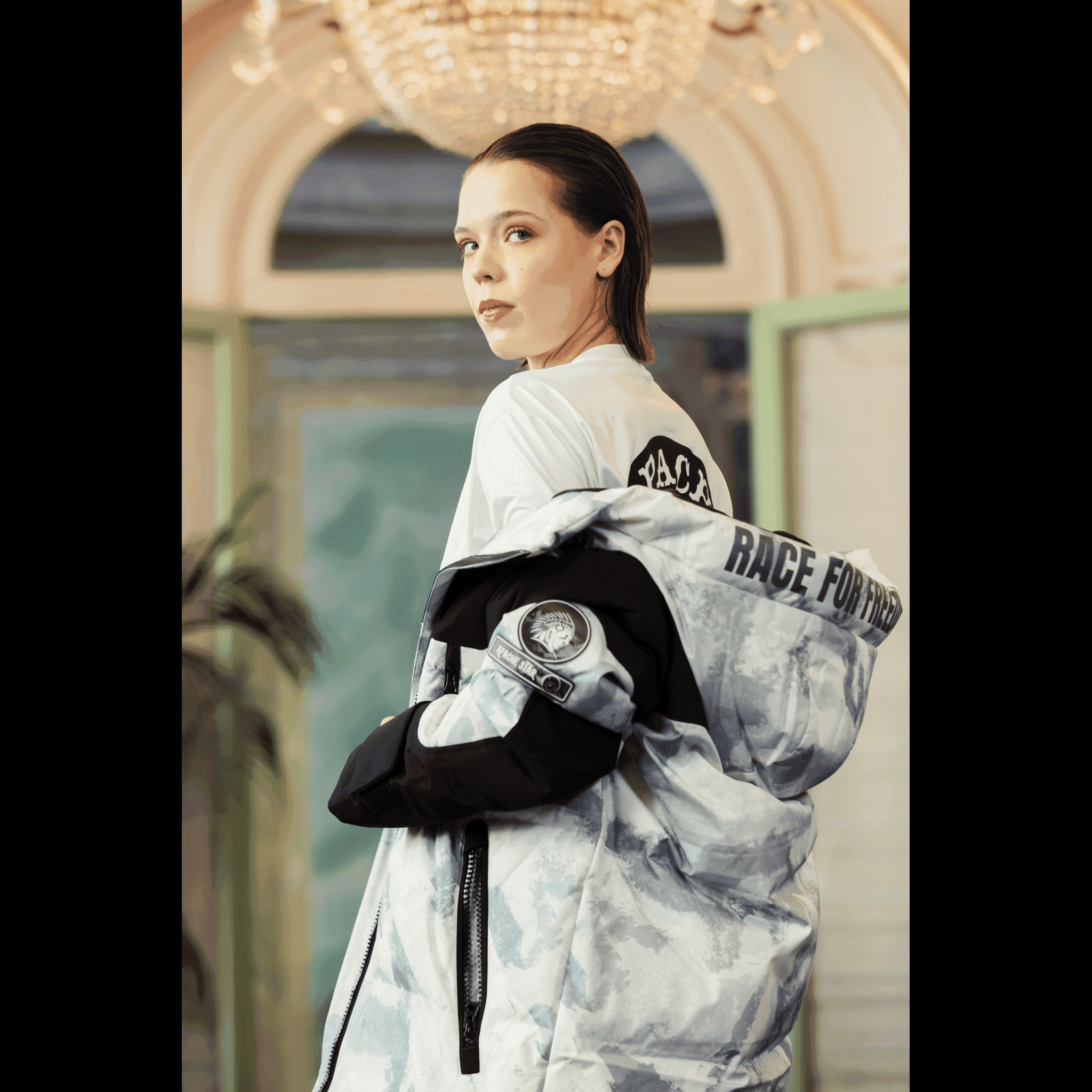 Female model showcasing back and sleeve details of Submerged Sentry by APACHE STAR white down coat at Paris Fashion Week, featuring bold 'Race for Freedom' text and logo patch.
