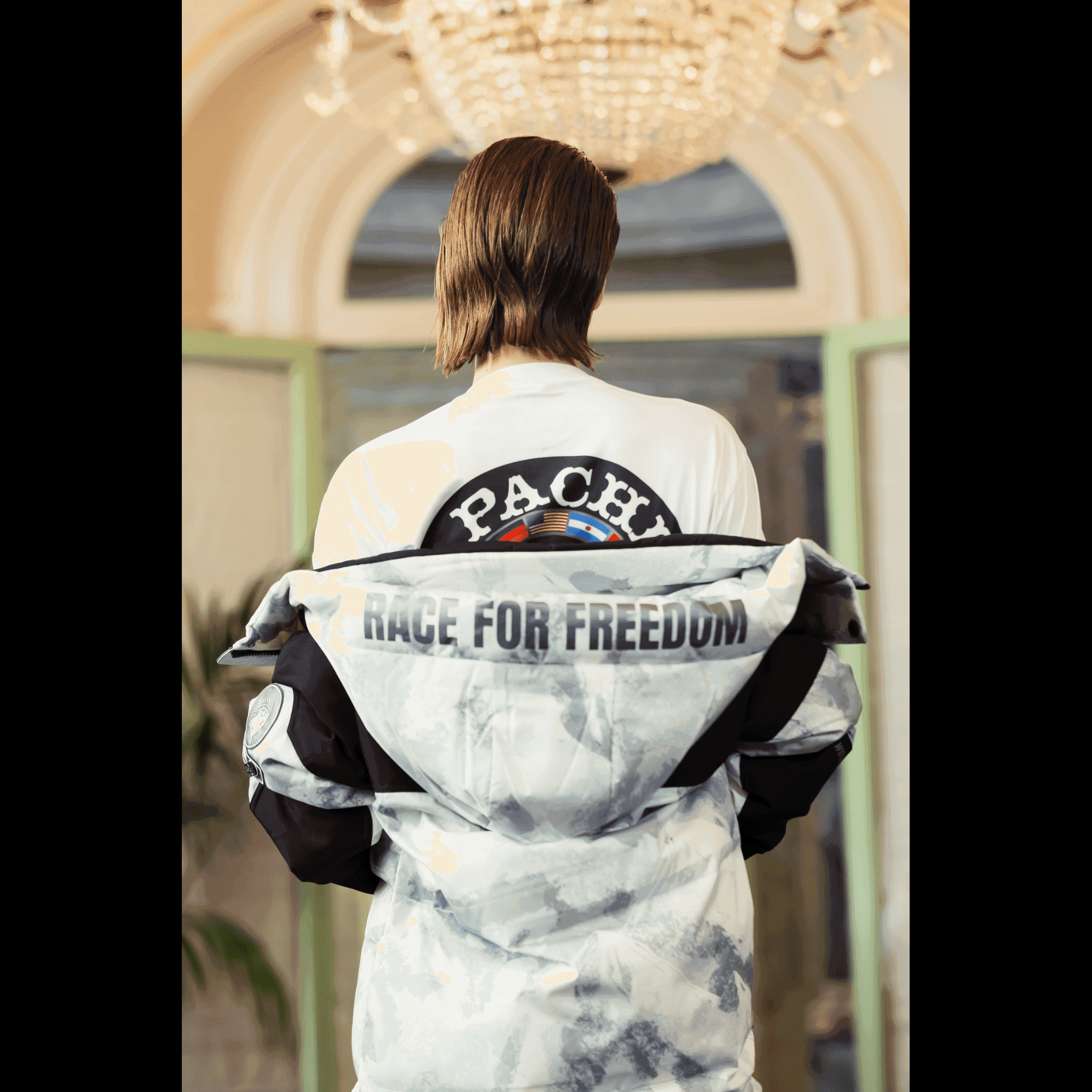 Male model wearing Submerged Sentry white down coat by APACHE STAR draped over shoulders at Paris Fashion Week, revealing 'Race for Freedom' and APACHE STAR back design.