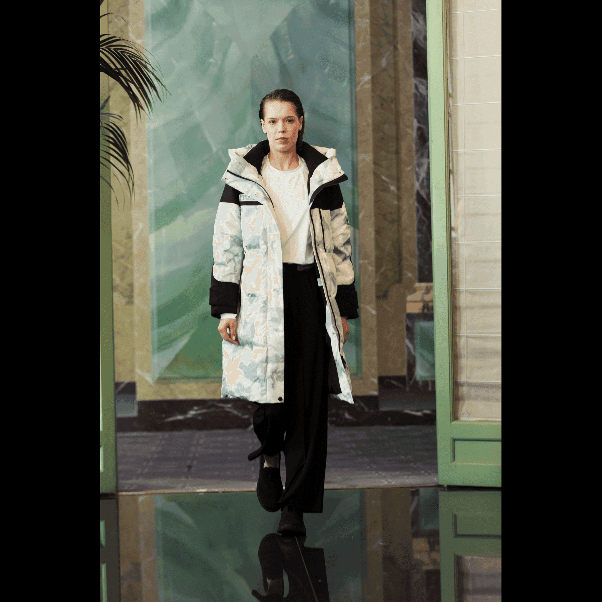 Model walking in Submerged Sentry white down coat by APACHE STAR at Paris Fashion Week, styled with black pants for a modern winter fashion statement.