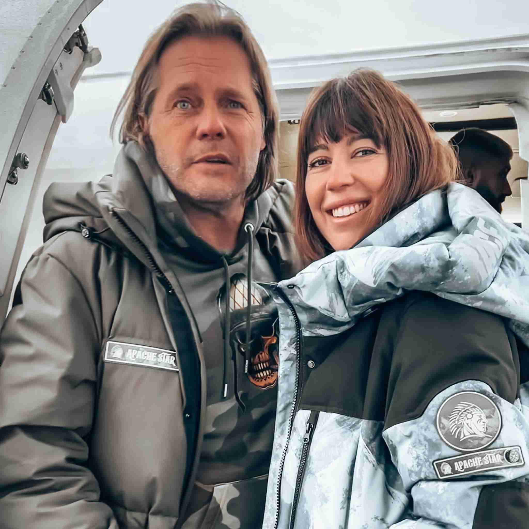 Vintage Down Coat - Blue Camouflage | Function, Style, Tech. Brand Owners Roger Klüh & Jessica Frühbrodt smiling in front of private jet, both wearing APACHE STAR down coats with visible branding.