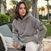 Woman wearing Iconic Dubai Hoodie by APACHE STAR in heather grey, lounging outdoors in a luxury resort setting. Features compass patch on sleeve.