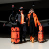 Fashionable travelers with APACHE STAR® Heritage Trunk Set in Apache Orange, showcasing luxury suitcase travel set in an aviation-hangar.